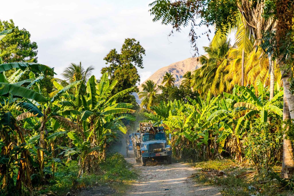 Dusty jungle roads are slowly navigated by two water drilling trucks.