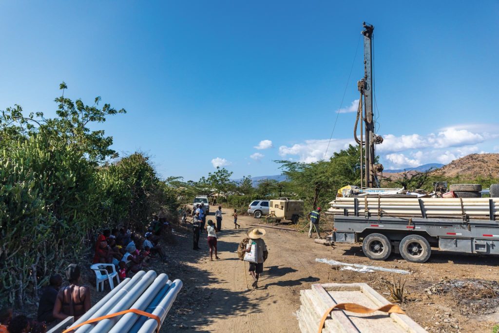 Local villagers gather along the road as workers drill a well near Terre Blanche, Haiti.