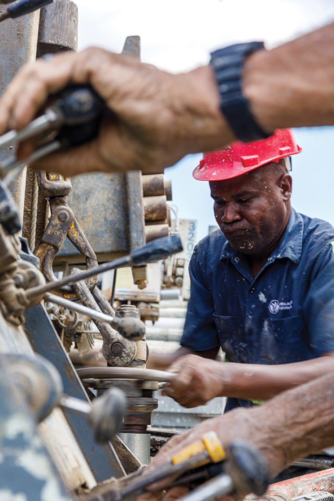 Haitian well driller in red hard hat, tightening a wheel on drilling rig.