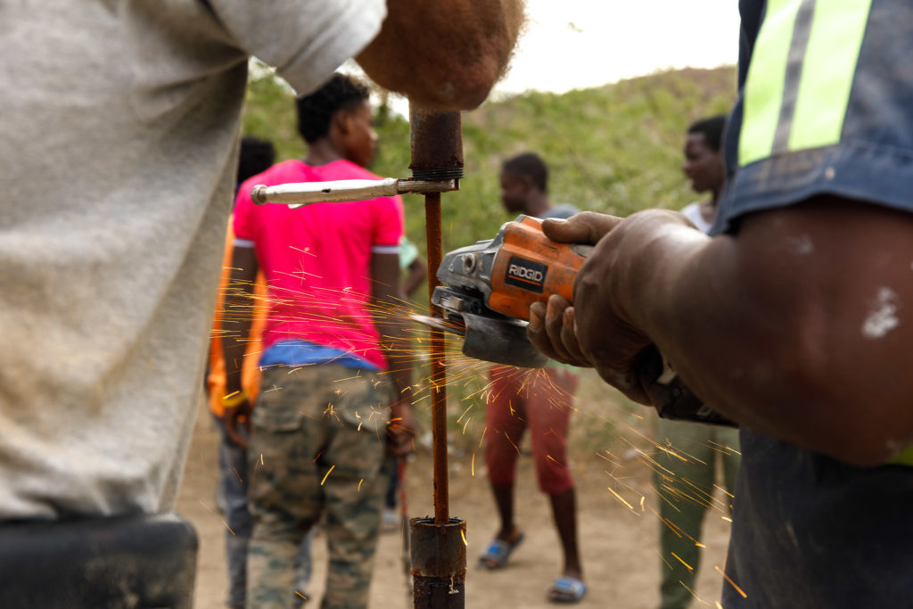 A Haitian worker cuts rusty old steel cable while repairing a water well.