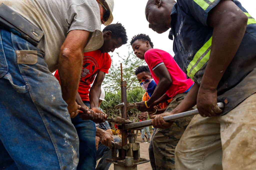 Six men use tools to lift a rusting metal pipe out of a water well near Terre Blanche, Haiti.