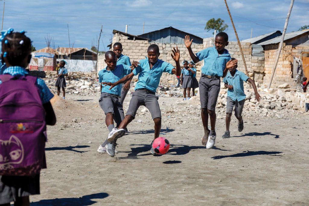 Young Haitian school students in grey and blue uniforms battle for a soccer ball during recess in Gonaieves, Haiti.