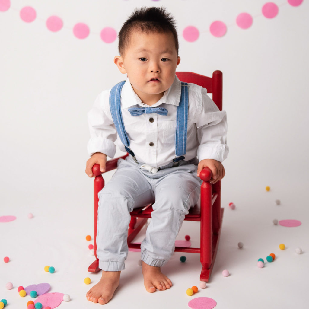 Young Asian boy with Downs Syndrome sitting barfoot in red rocking chair.