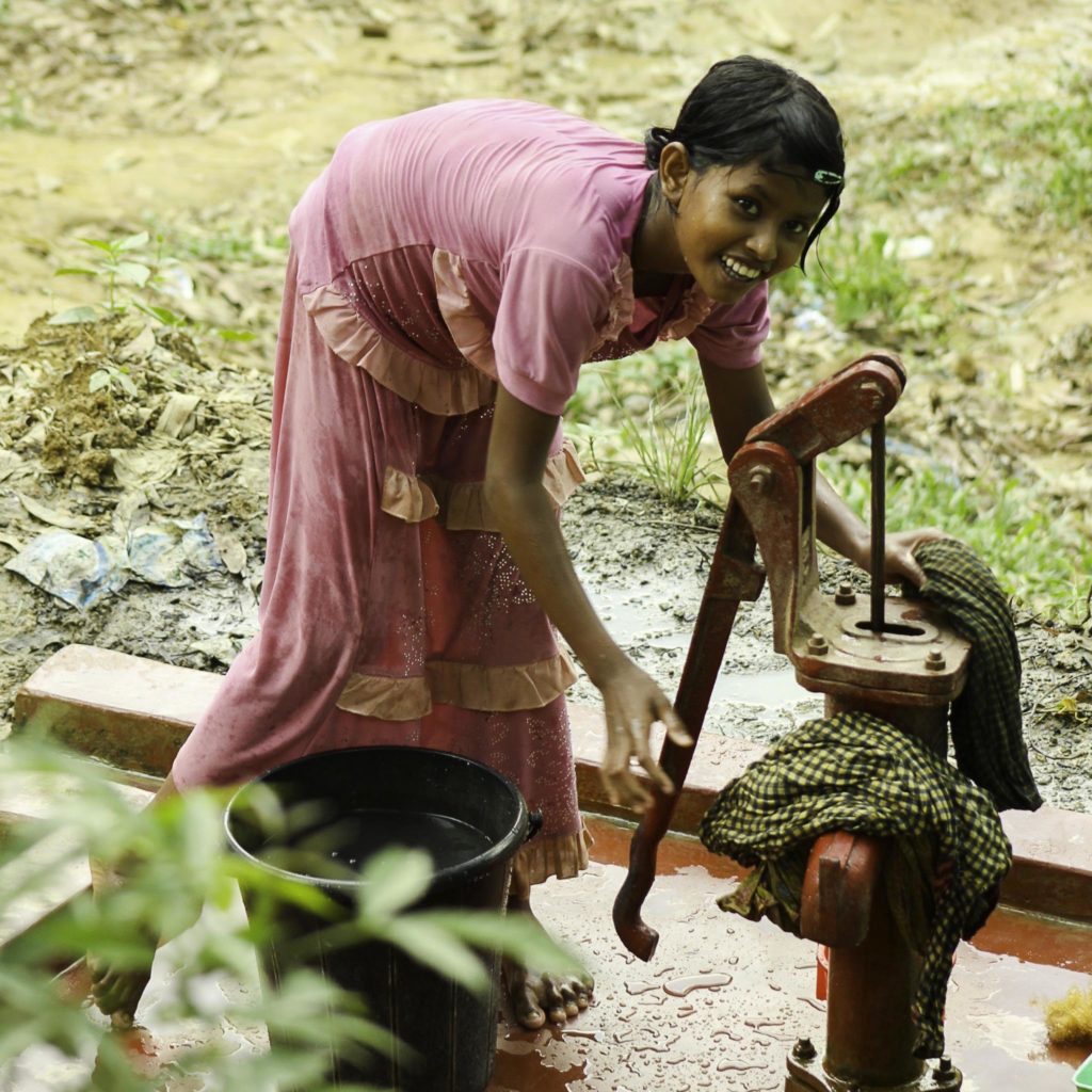 Smiling young girl draws water from a hand pump for washing in Bangladesh