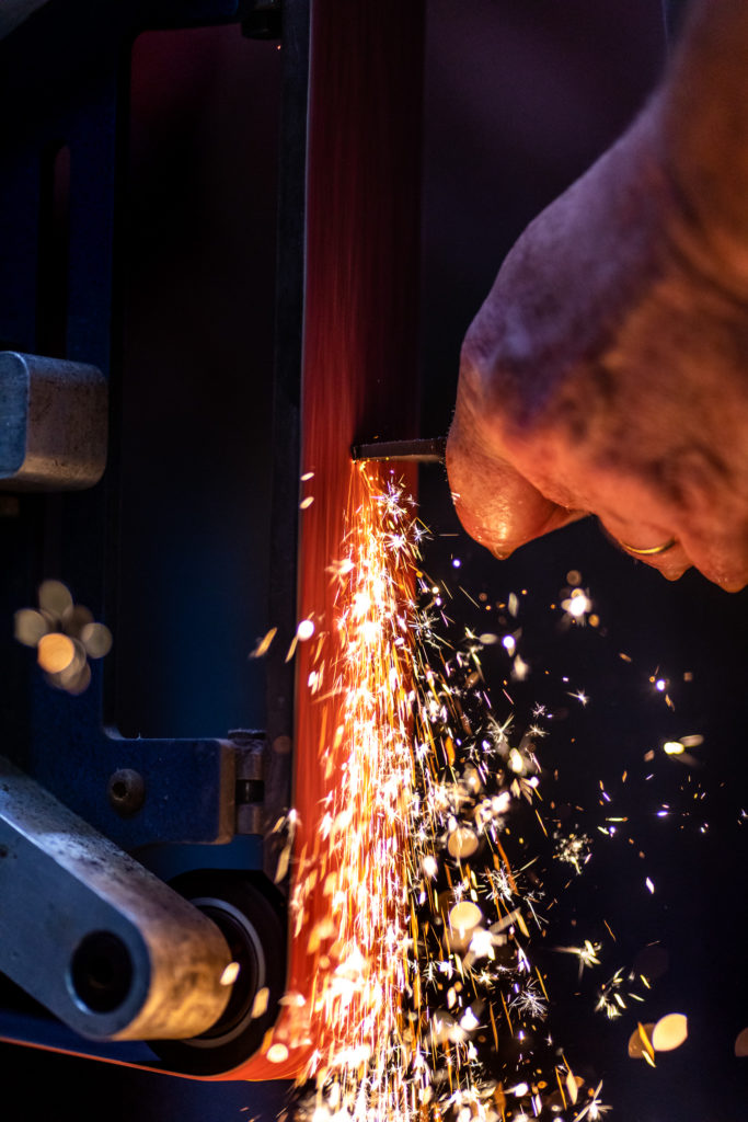 Sparks fly from a grinder as the handle of a knife is ground smooth.