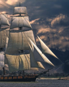 A wooden ship with three masts sailing under cloudy skies.