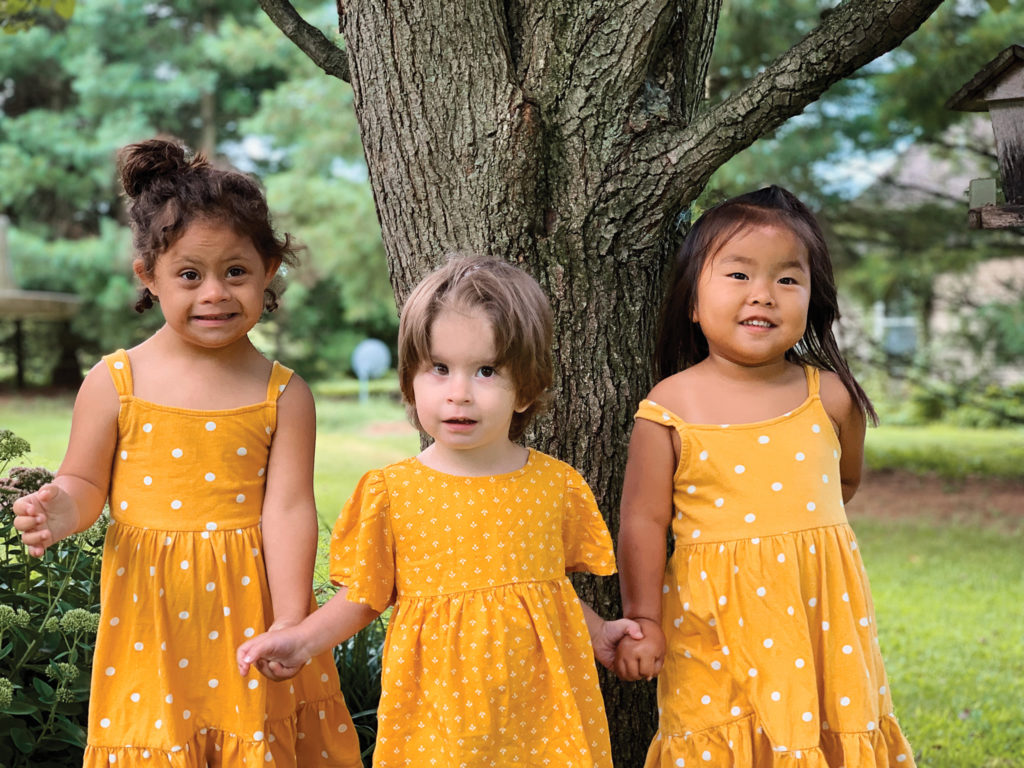 Young girls in bright yellow dress holding hands smiling in front of a tree.