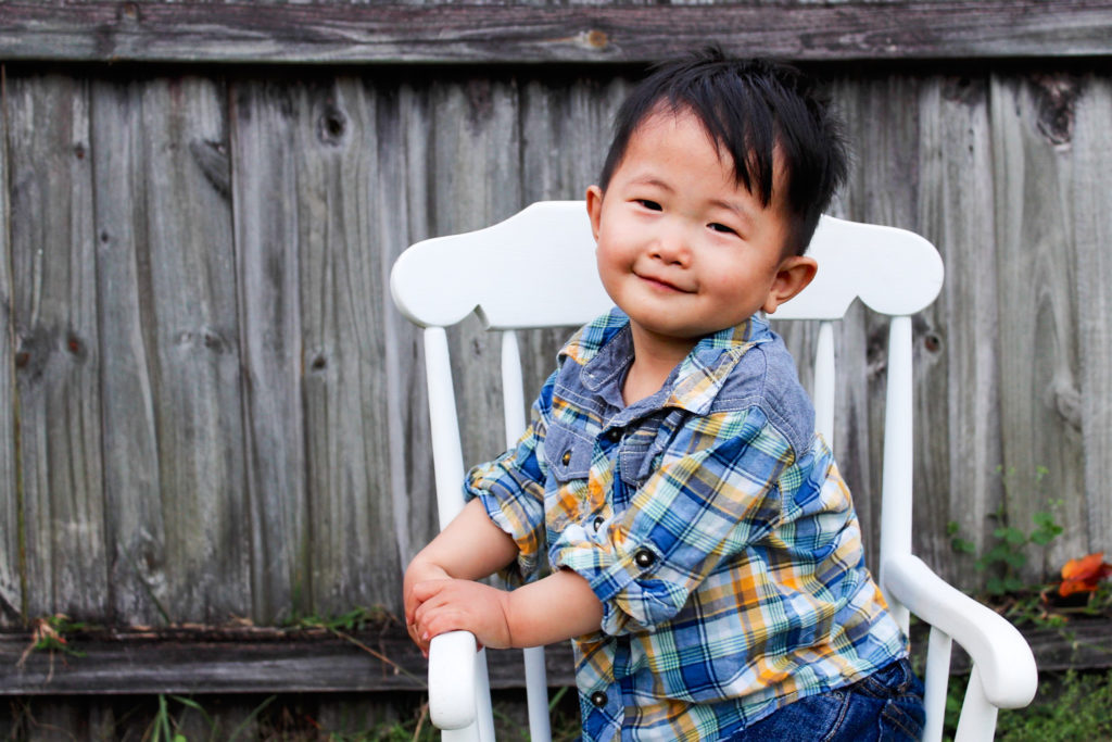 Smiling young boy sitting on white rocking chair.