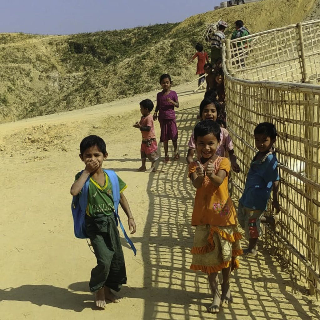 Young boys and girls in bright clothes pose and smile for a Plain Compassoin worker.