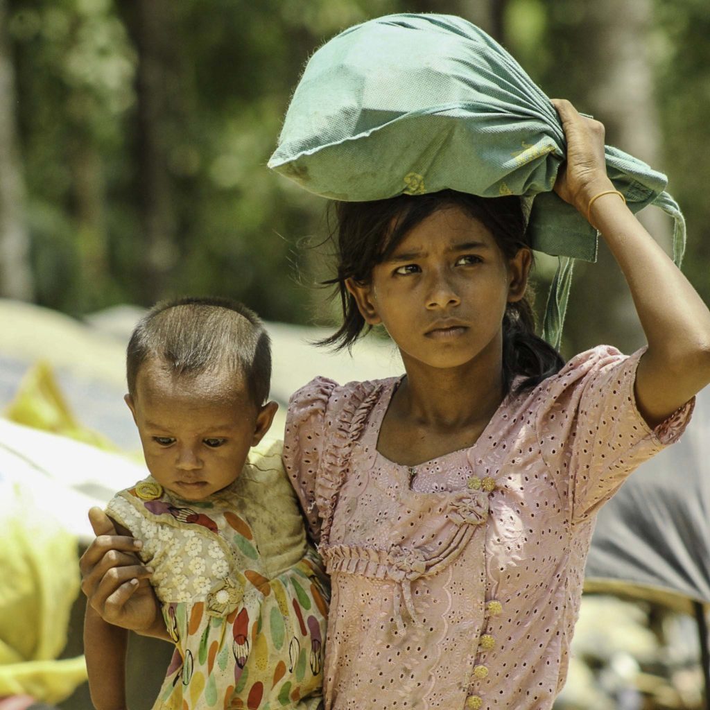 A young girl sheilds her eyes with a bag while holding a baby on her hip.