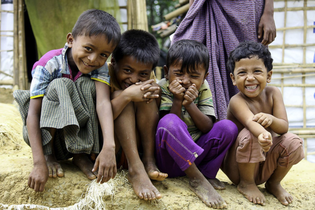 Four children sitting close to each other, barefoot on a bank giggling and laughing.