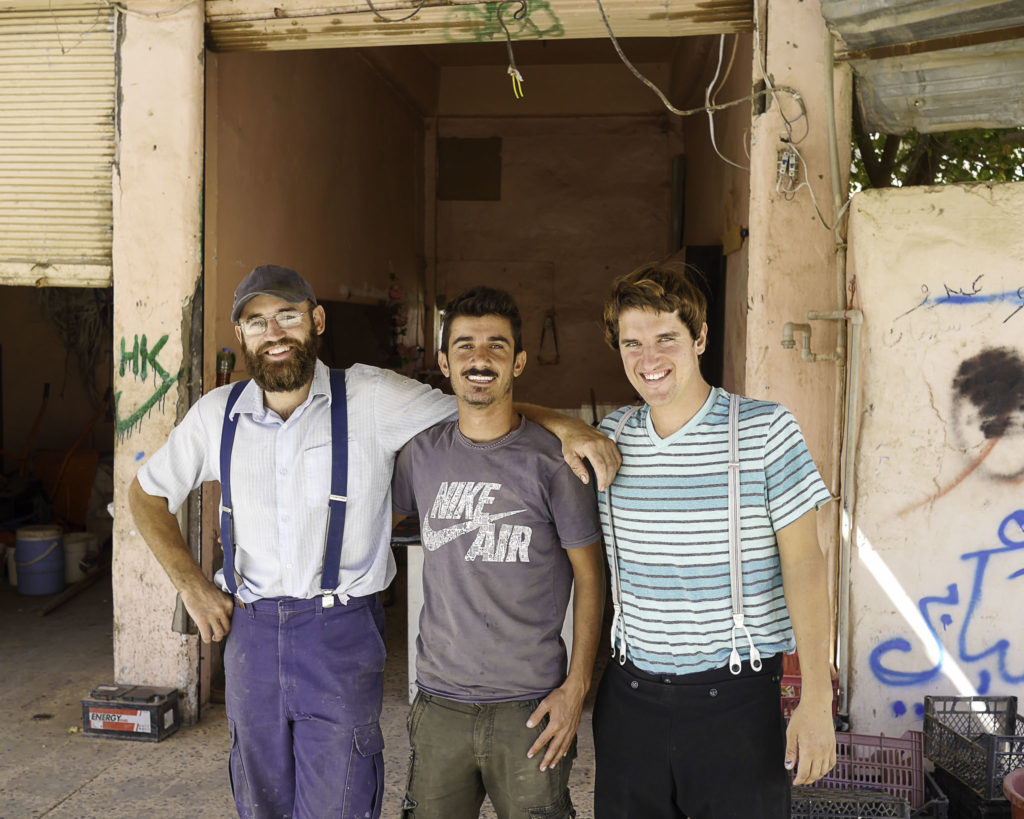 Two Plain Comapssion workers wearing suspenders pose with a local.
