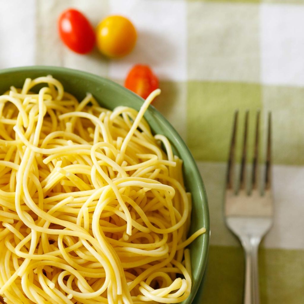 bowl spaghetti noodles, green bowl, fork, sliced cherry tomatoes, checkered table cloth