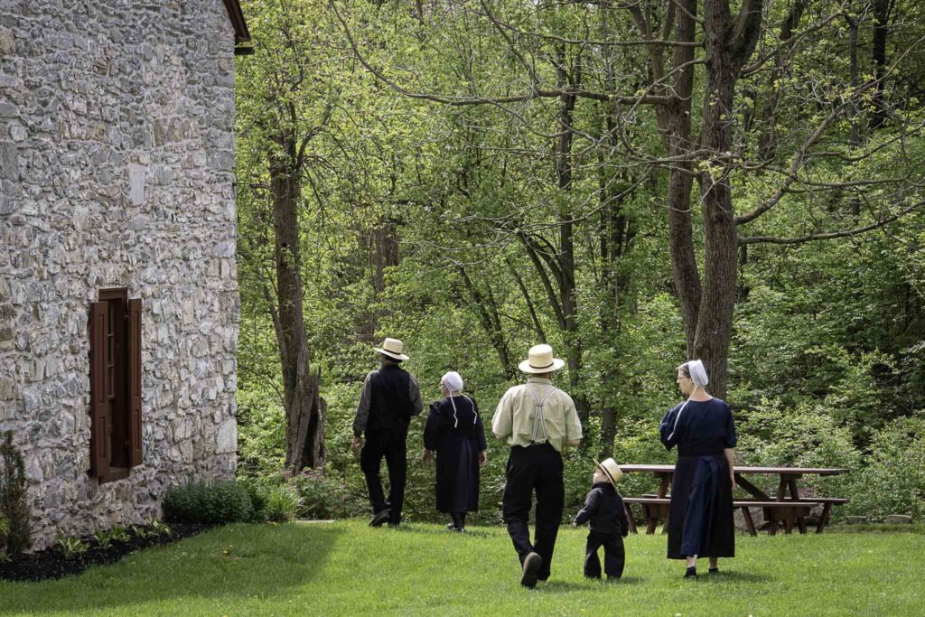 Amish Men and women along with a child walk around the Stoltzfus Homestead in summer.