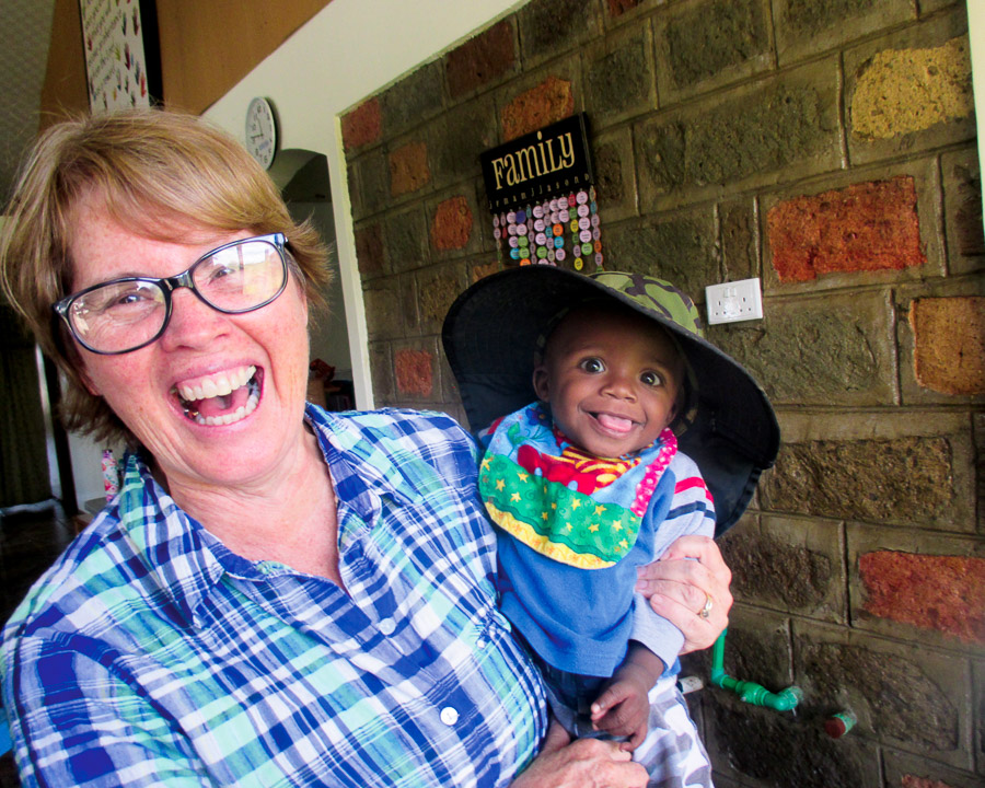 A female volunteer laughing while holding a cute baby with an oversized camo hat at Family Key's International.