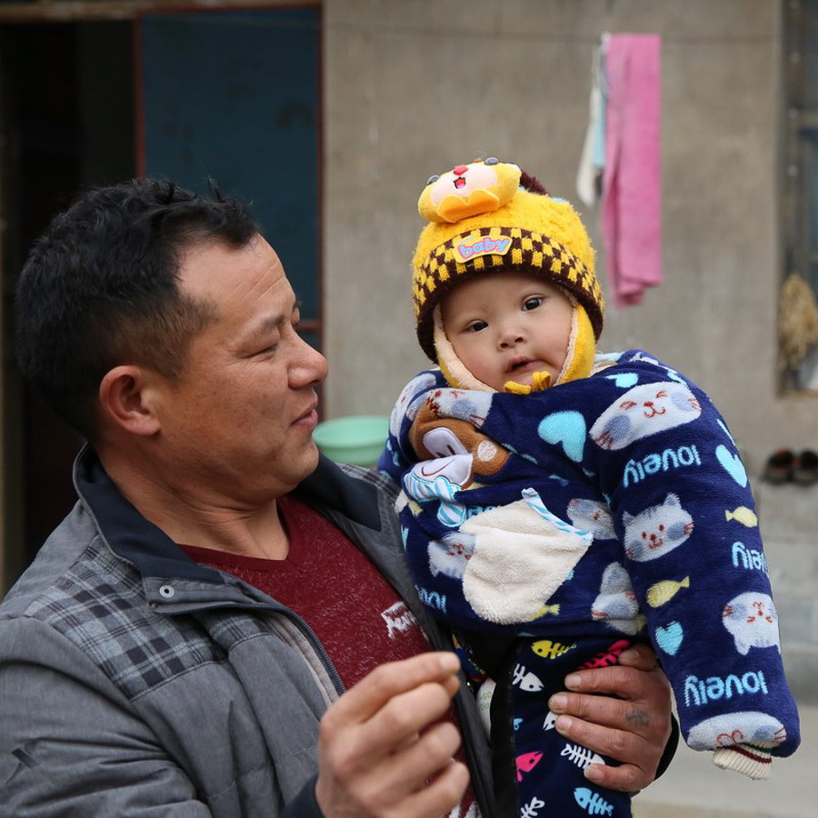 A middleaged Asian father holds a child, both dressed in warm winter clothing.