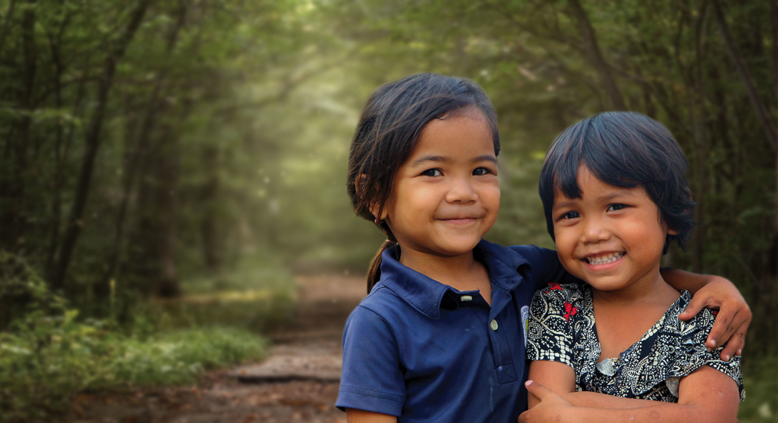 Two impoverished little girls with smiling faces on a jungle path