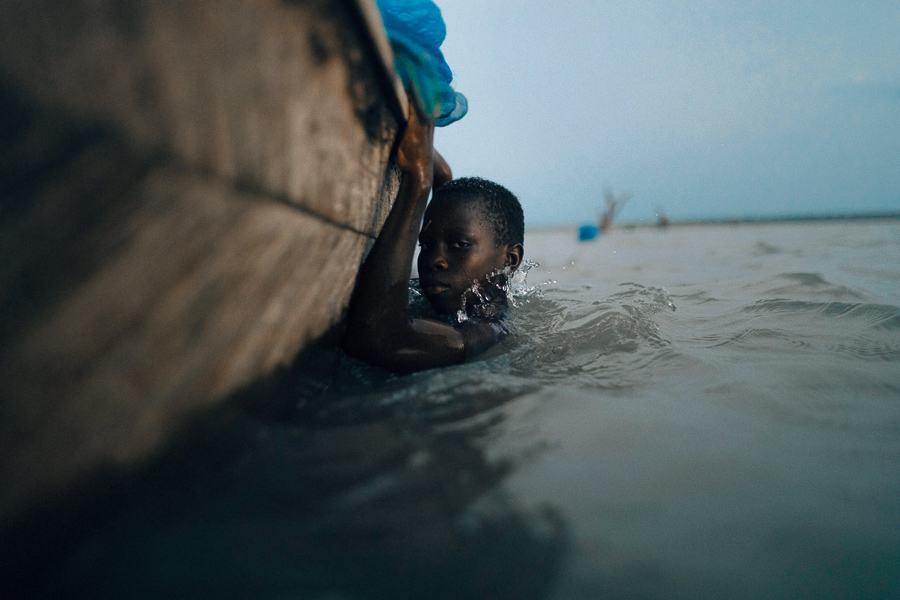 A young African child hangs onto the side of a wooden fishing boat.