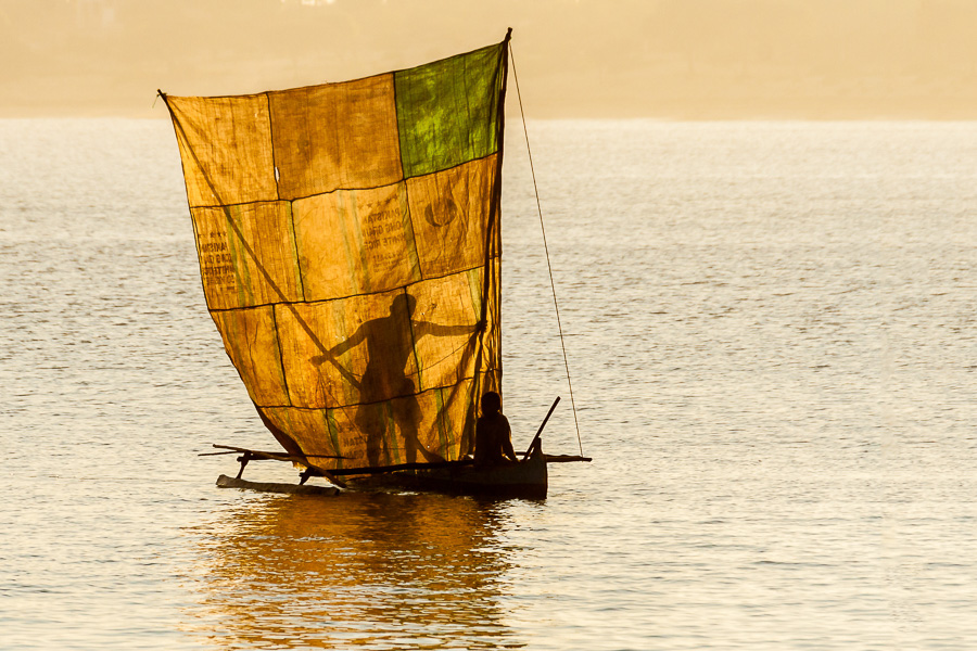 A fisherman and his son work on a boat with a single outrigger on a bright day.