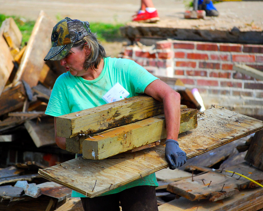 A woman carries wood scraps as clean up begins on a home damaged by a storm.