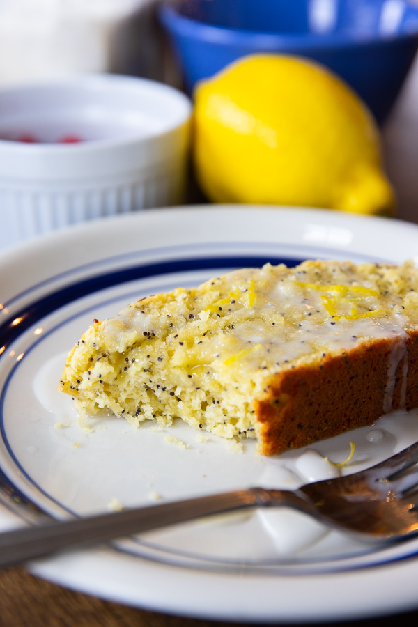 A slice of lemon poppyseed bread, drizzled with frosting on a white plate with a bit taken out of the end.