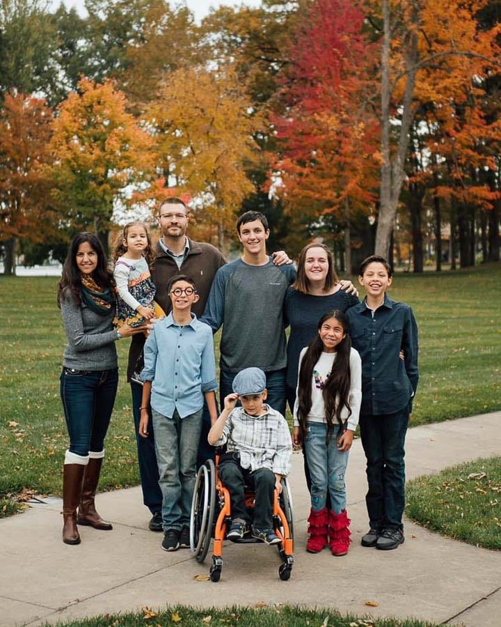 All members of the gagnon family pose for a fall family portrait on concrete sidewalks with beautiful yellow, red, and orange tree's behind them.