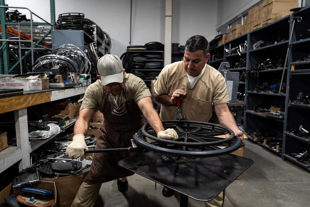 Two men in brown uniforms work to repair a used wheelchair