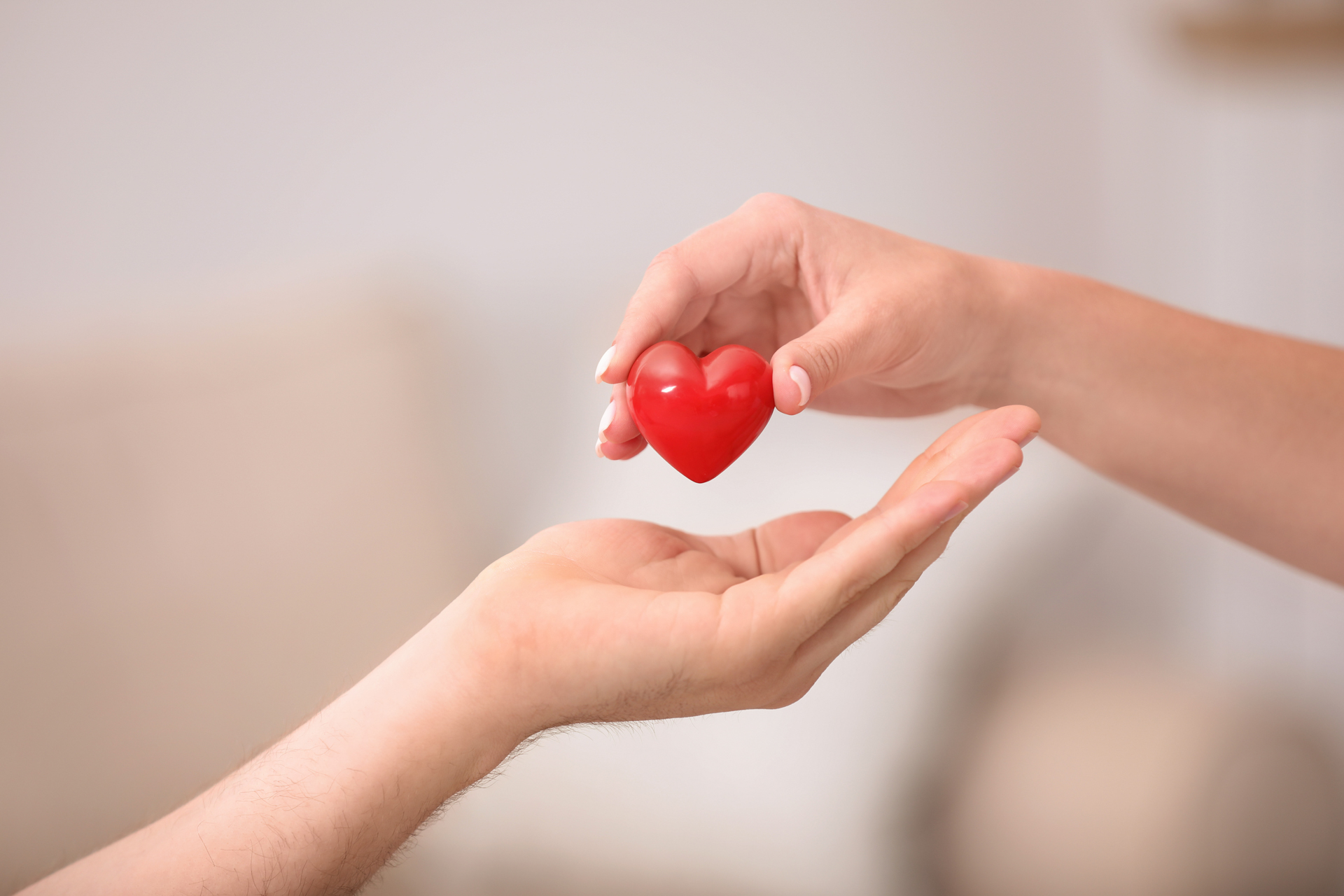 Person giving red heart to another on a blurred background, closeup.