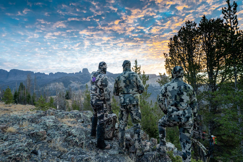 Three elk hunters wearing camouflage standing at the edge of a mountain in the Colorado Rockies
