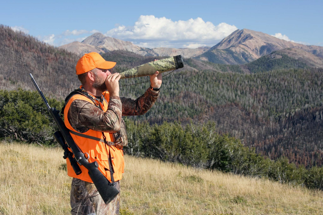 Hunter blowing an elk bugle with mountains in the background